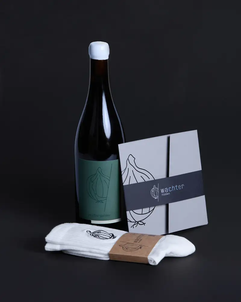 Das perfekte Geschenk – unser Set aus hochwertigem Gutschein, limitierten Wachter-Foodbar-Socken und einer Flasche unseres Wachter Foodbar Weins vom Weingut Daniel Mattern ist eine Einladung zum Genießen – ob für andere oder für sich selbst.
